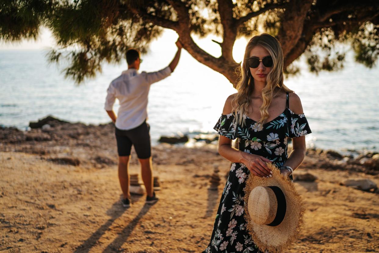 Loving young couple by the tree on coastline at summer sunset after arguing