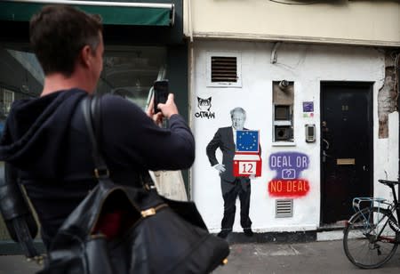 A man takes a photograph of a mural depicting Britain's Prime Minister Boris Johnson on the side of a residential building in London