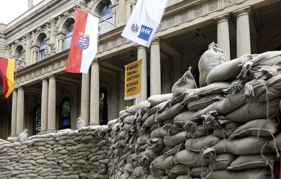 Protesters have build a wall around the Frankfurt stock exchange with sandbags to demonstrate against speculations in Frankfurt, central Germany, Sunday June 17, 2012. Poster in center reads: Transaction Tax Now. Activists calling for a tax on financial transactions have erected a wall of sandbags outside the Frankfurt stock exchange. The anti-globalization group Attac said that about 200 people participated in Sunday’s action. Carrying placards with slogans such as “Stem Speculation” and “Financial transaction tax now,” they built the wall of sandbags around the statues of a bull and a bear symbols of optimistic and pessimistic markets that stand in front of the exchange building. Flags from left: teh German flag, the flag of Hesse State and the flag with the logo og teh Chamber of Commerce. (AP Photo/dapd/Mario Vedder)