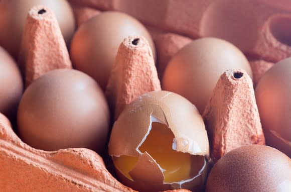 Close-up of eggs in a carton; one of them is cracked and the yolk is showing.