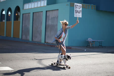 Kristen Schonert skateboards past a Snap Inc. office with a protest sign in Venice, a beach community of Los Angeles, California, U.S., March 2, 2017. REUTERS/Lucy Nicholson