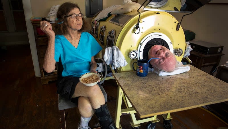 In this Friday, April 27, 2018, photo, attorney Paul Alexander chats with caregiver and friend Kathryn Gaines as he drinks coffee and she eats breakfast beside his iron lung at his home in Dallas. Alexander died Monday, March 11, 2024, at a Dallas hospital, said Daniel Spinks, a longtime friend. He said Alexander had recently been hospitalized after being diagnosed with COVID-19 but did not know the cause of death.