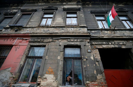 A woman peers out a window of a dilapidated building that shows bullet marks from the 1956 anti-Communist uprising, with the revolutionary flag posted on the front, insignia removed, in Budapest, Hungary, October 20, 2016. REUTERS/Laszlo Balogh