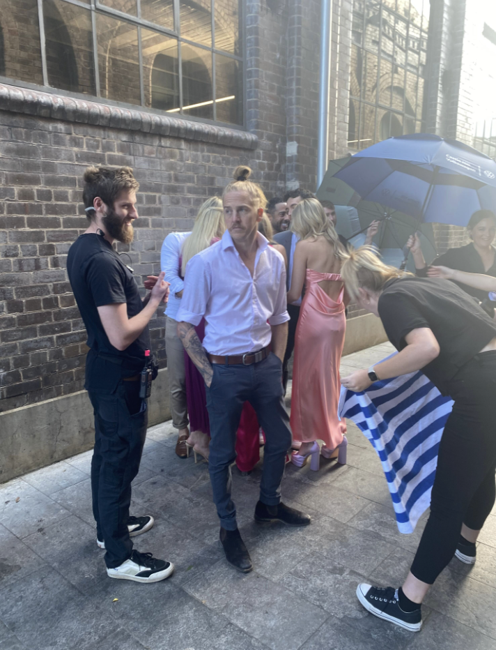 MAFS' Cameron stands with his hands in his pockets while a producer nearby gets a towel ready. 