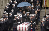 Shannon Slutman, center, stands under an umbrella while military and fire officials salute the casket of her husband, U.S. Marine Corps Staff Sergeant and FDNY Firefighter Christopher Slutman, as it leaves St. Thomas Episcopal Church, Friday April 26, 2019, in New York. The father of three died April 8 near Bagram Airfield U.S military base in Afghanistan. (AP Photo/Bebeto Matthews)