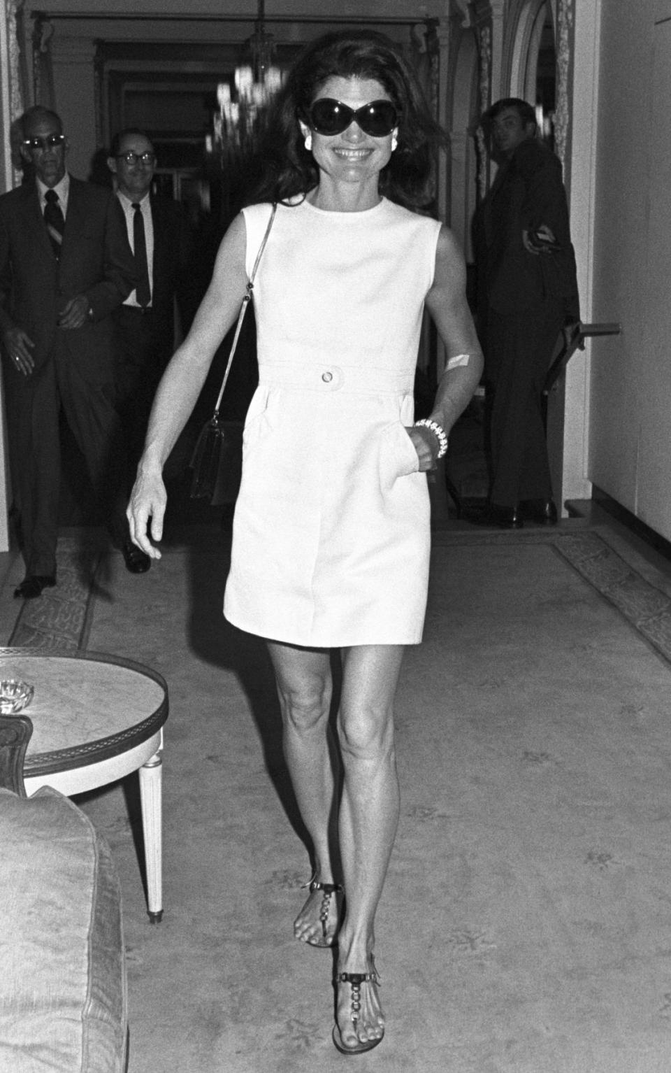 Jacqueline Kennedy Onassis wearing a short sleeveless white dress and sunglasses circa 1970