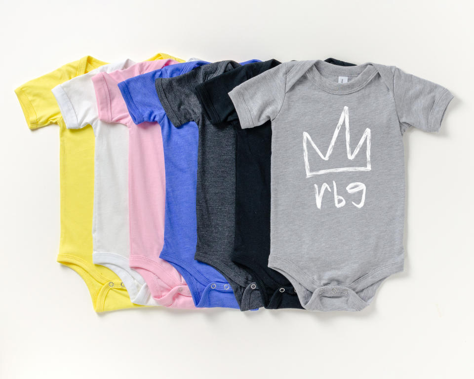 This image shows a variety of onesies with a line drawing of a crown and the initials “rbg” in lowercase lettering. Twenty percent of proceeds will be donated to the ACLU's Women's Rights Project. (Lizzy Russinko via AP)