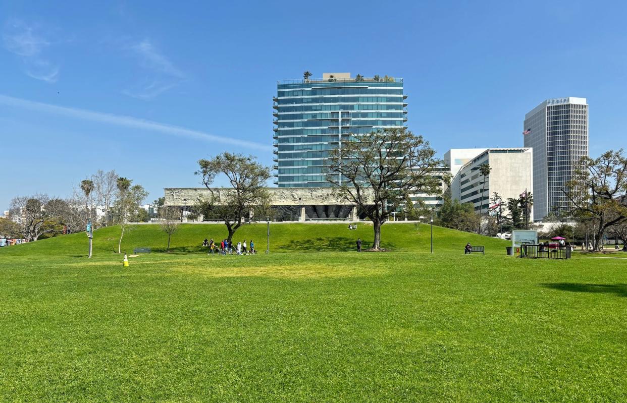 The La Brea tar pits museum with tall buildings around it and a lawn in front