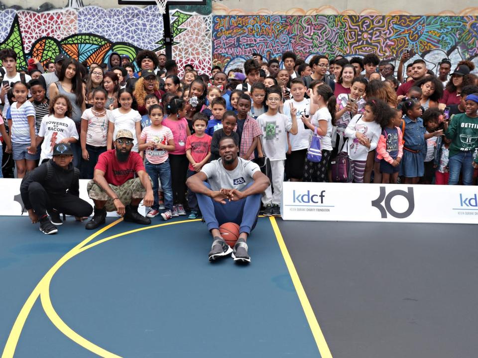 Kevin Durant poses in front of a large group of kids on a basketball court in 2017.