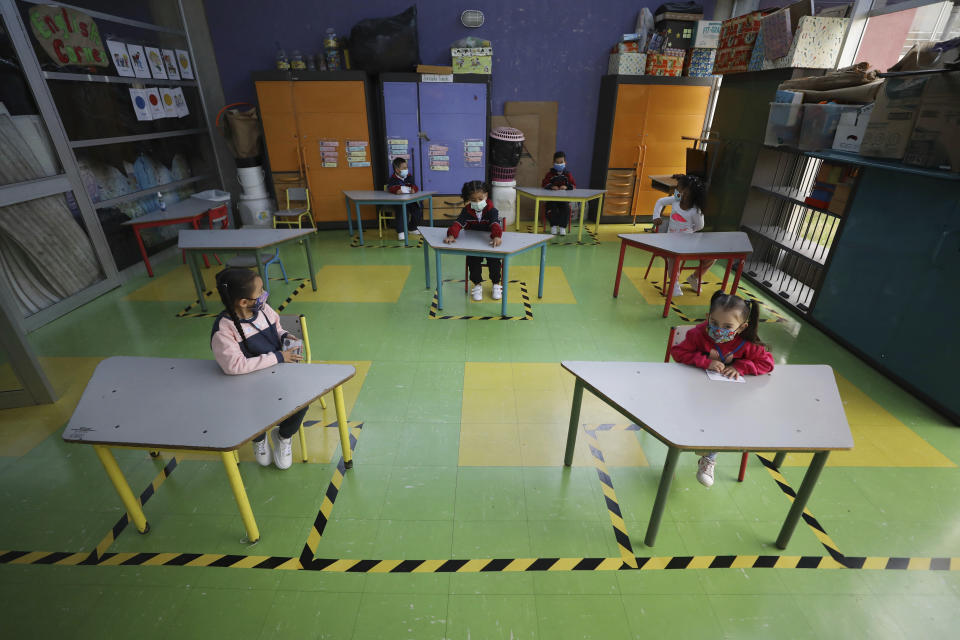 Preschool students wear masks and sit at socially distanced desks to prevent the spread of new coronavirus on their first day back to in-person class in Bogota, Colombia, Monday, Feb. 15, 2021. Bogota is returning students to classes on alternating days at public schools after a year of online education due to the pandemic. (AP Photo/Fernando Vergara)