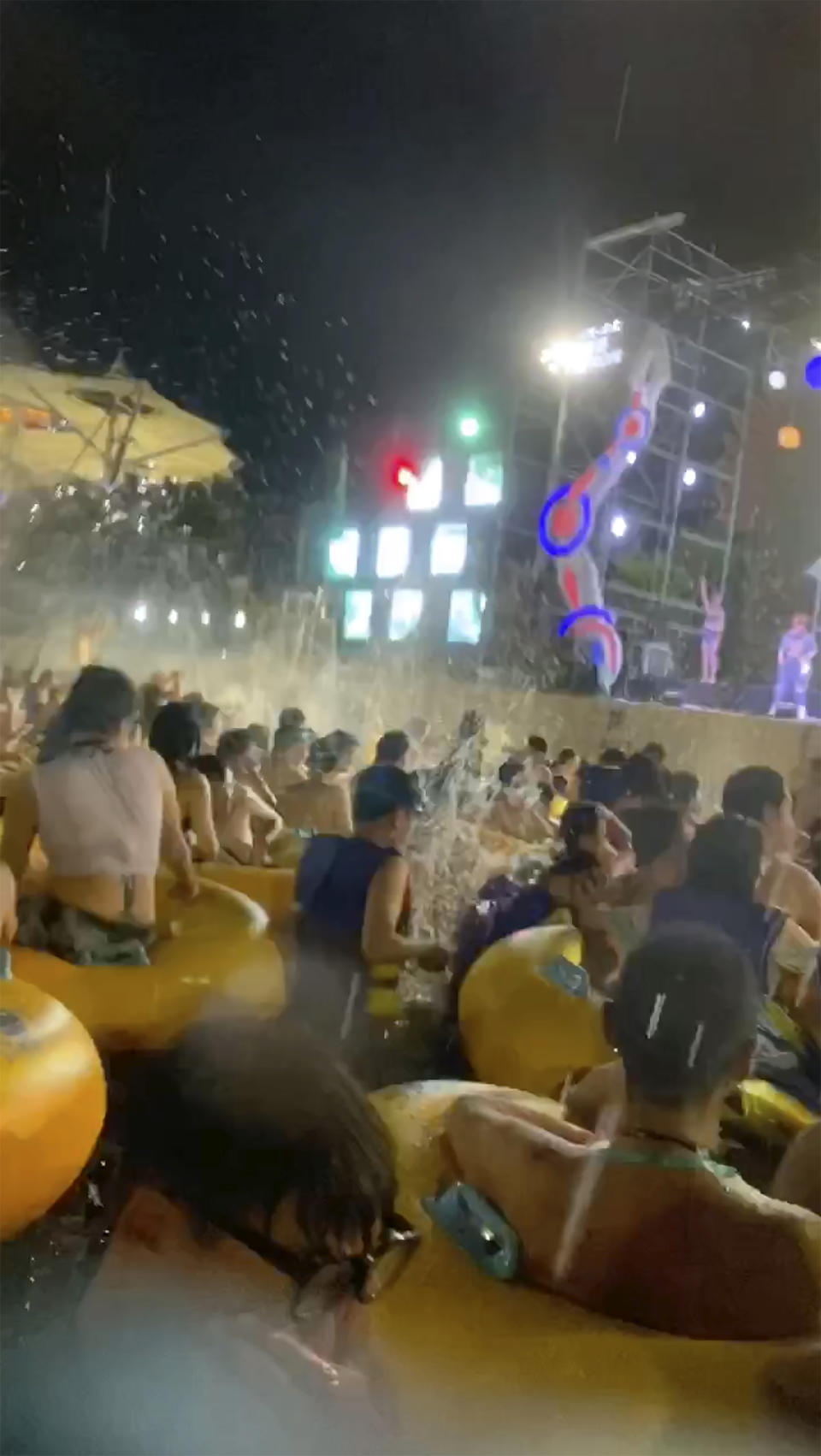 This image made from an Aug 3, 2020 video shows crowd gather in a pool as they watch performers on a stage at Wuhan Maya Beach Water Park in Wuhan, central China. For more than two months, the 11 million residents of Wuhan endured a strict lockdown as coronavirus raced around the city. Now, some are letting loose en masse at rocking nighttime pool parties at the popular amusement park chain. The park reopened in late June, and the crowds have picked up in August. (anonymous photo via AP)