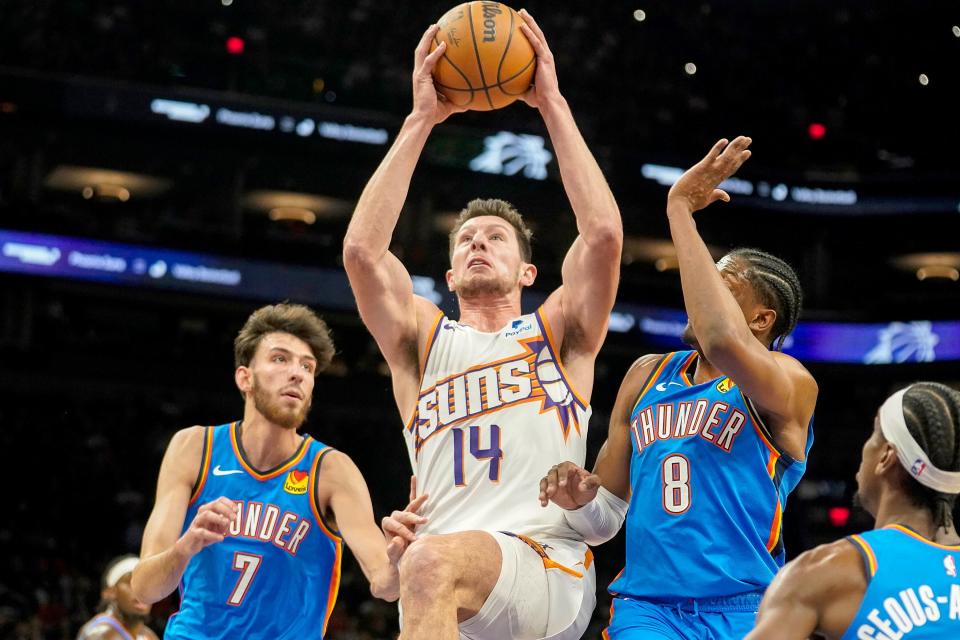 Phoenix Suns' Drew Eubanks (14) goes to the basket between Oklahoma City Thunders' Chet Holmgren (7) and Jalen Williams (8) during the first half of an NBA basketball game in Phoenix, Sunday, Nov. 12, 2023.