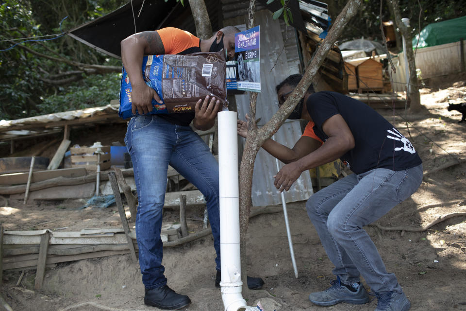 Volunteers from Animal Heart Protectors fill a dispenser with food for cats on Furtada Island, popularly known as “Island of the Cats,” in Mangaratiba, Brazil, Tuesday, Oct. 13, 2020. Volunteers are working to ensure the stray and feral cats living off the coast of Brazil have enough food after fishermen saw the animals eating others' corpses, an unexpected consequence of the coronavirus pandemic after restrictions forced people to quarantine, sunk tourism, shut restaurants that dish up seafood and sharply cut down boat traffic around the island. (AP Photo/Silvia Izquierdo)