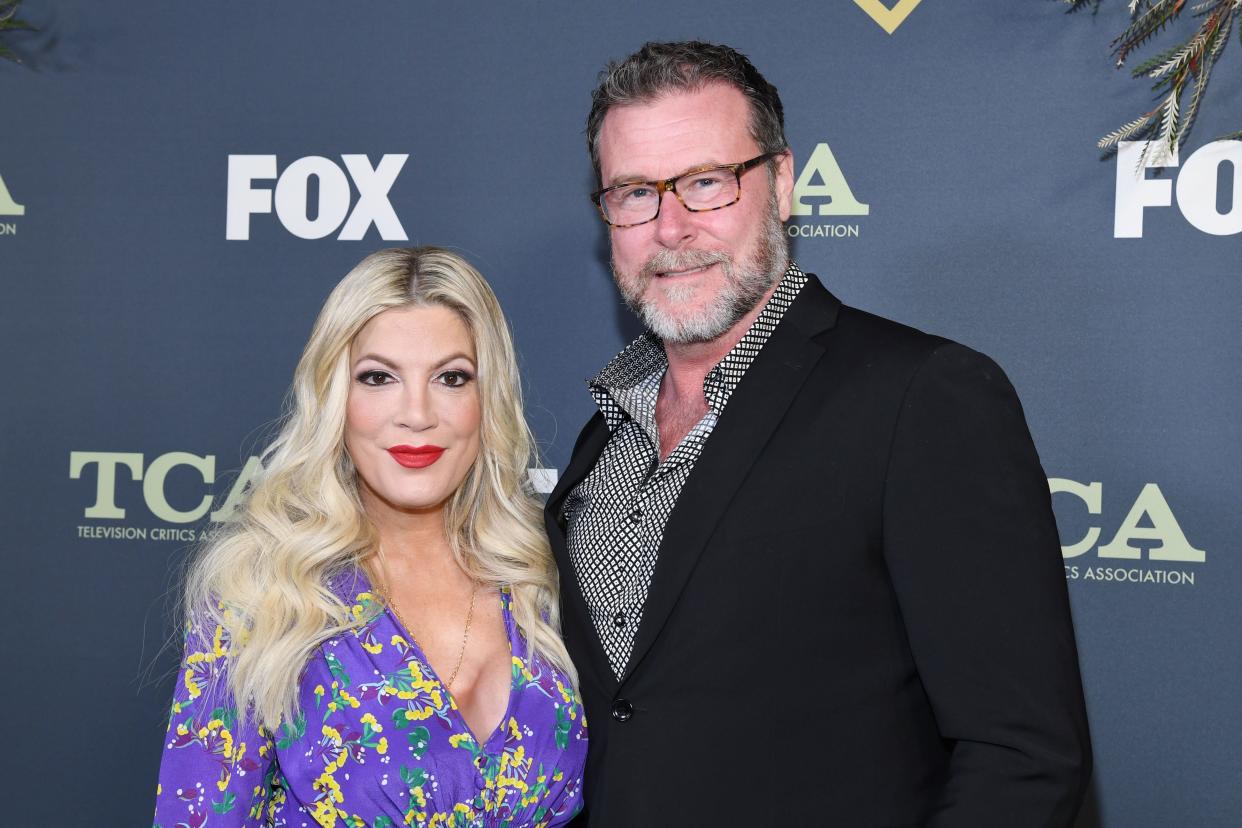 Tori Spelling in a purple blouse smiles with husband Dean McDermott in a black jacket on the carpet