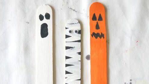 three painted craft stick puppets resembling ghost, mummy, and jackolantern for halloween puppet show activity