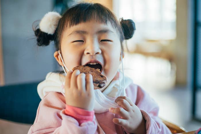 Young girl with pigtails eating a cookie, smiling with eyes closed