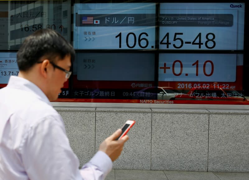 A man checks his phone as he walks past a display of market indices including the dollar to yen exchange rate in Tokyo, Japan, May 2, 2016. REUTERS/Thomas Peter