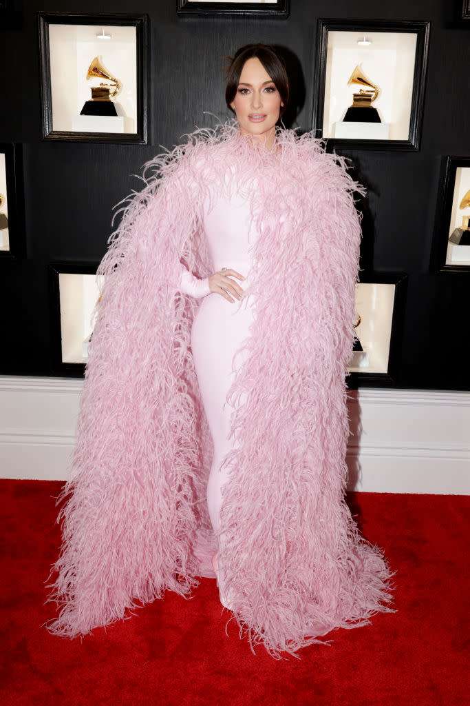 Kacey Musgraves in pale pink gown with oversized ostrich cape.