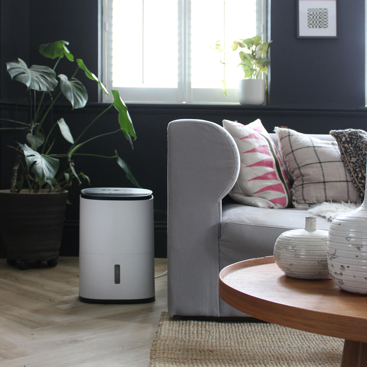  A Meaco dehumidifier by the side of a sofa in a living room with dark walls. 