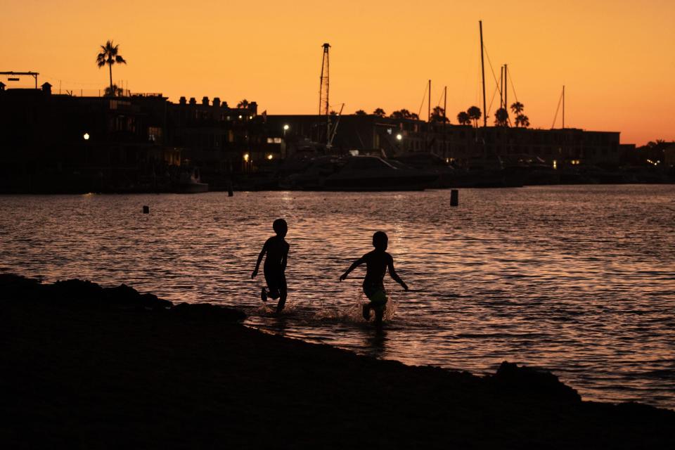 File: Amid a golden sky, youngsters run in the water on a warm summer evening at dusk at Marina Park in Newport Beach.