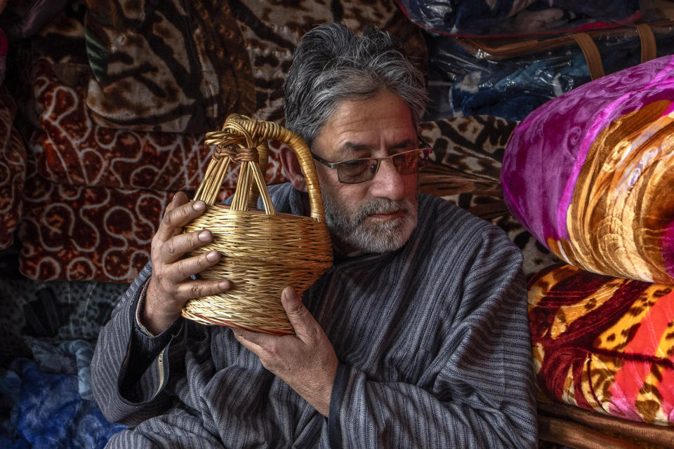 Mohammad Shafa, a Kashmiri shopkeeper selling blankets, poses with a traditional fire port called kangri, warming his ears in Srinagar, Indian controlled Kashmir, Friday, Jan. 5, 2024. For locals, the major source of heat is the kanger, a pot filled with hot coal embers that is tucked inside their pheran, a traditional knee-length cloak. Almost ensnared by its warmth, people only step outside for work and other essentials. (AP Photo/Dar Yasin)