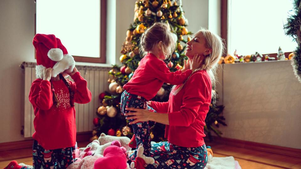 mother and daughters wearing matching christmas pajamas while playing under christmas tree