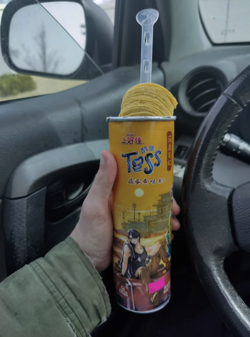 A hand holding a cylindrical pringles container with a plastic tab poking out to bring all the chips up