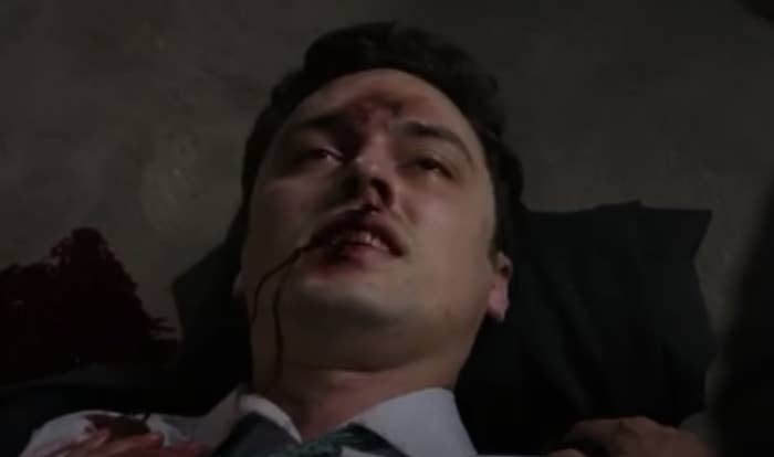 A man lays covered in blood, staring up with glazed eyes