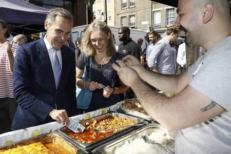 Bank of England governor Mark Carney tests a new polymer five pound note as he buys lunch at Whitecross Street Market in London, Britain September 13, 2016. REUTERS/Stefan Wermuth/File Photo