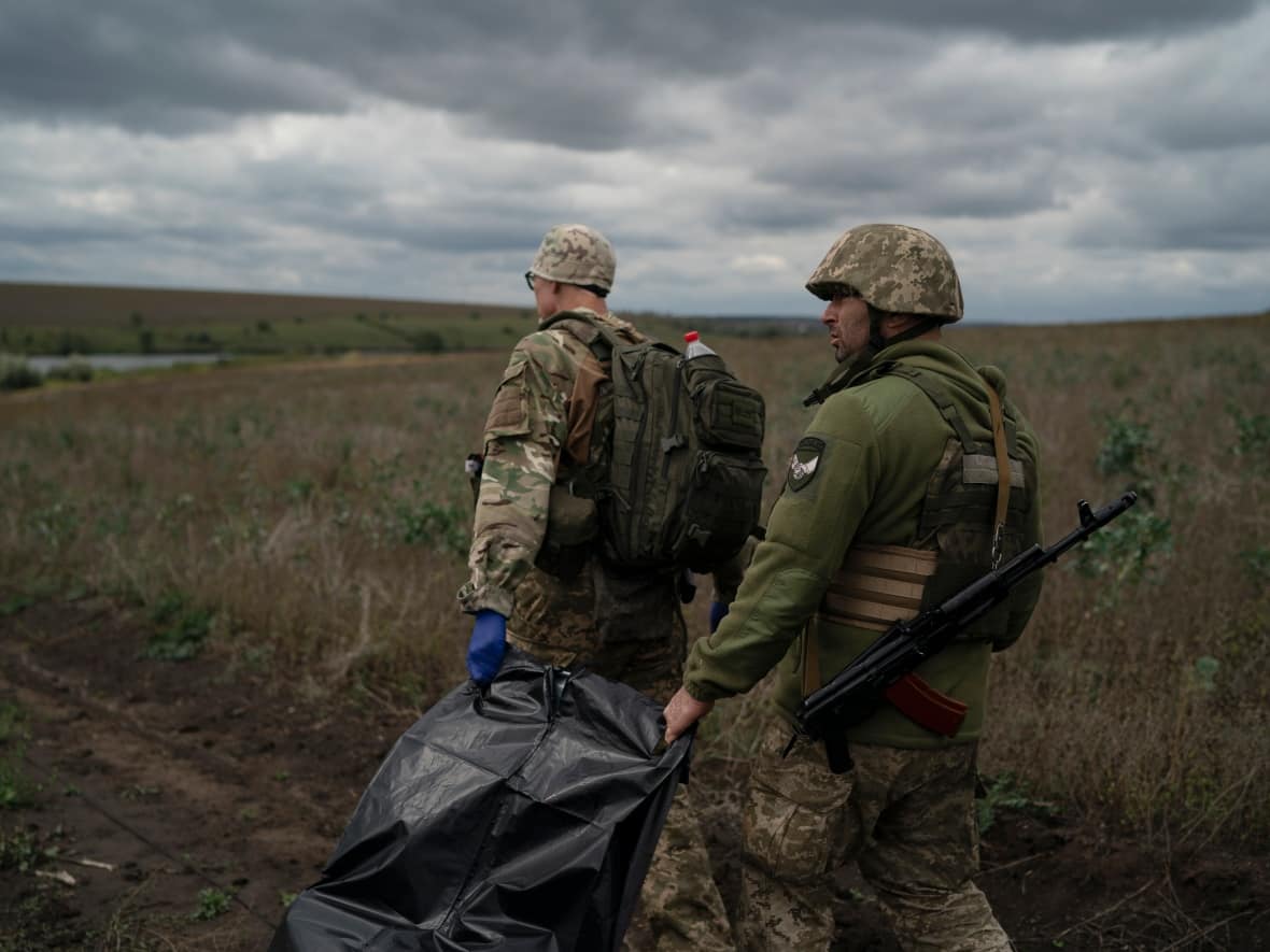 Ukrainian national guard servicemen carry a bag containing the body of a Ukrainian soldier in an area near the border with Russia in Kharkiv region, Ukraine, on Monday. (Leo Correa/The Associated Press - image credit)