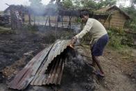 A villager removes sheets of tin from a fire after most homes were set on fire in ethnic violence at Khagrabari village, in the northeastern Indian state of Assam, Saturday, May 3 2014. Police in India arrested 22 people after separatist rebels went on a rampage, burning homes and killing dozens of Muslims in the worst outbreak of ethnic violence in the remote northeastern region in two years, officials said Saturday. (AP Photo/Anupam Nath)