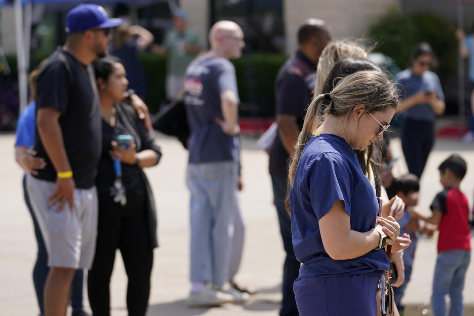 Visitors stand in silence at a makeshift memorial by the mall where several people were killed, Monday, May 8, 2023, in Allen, Texas. A person opened fire at the suburban Dallas shopping mall last weekend, killing eight people and wounding seven others.(AP Photo/Tony Gutierrez)