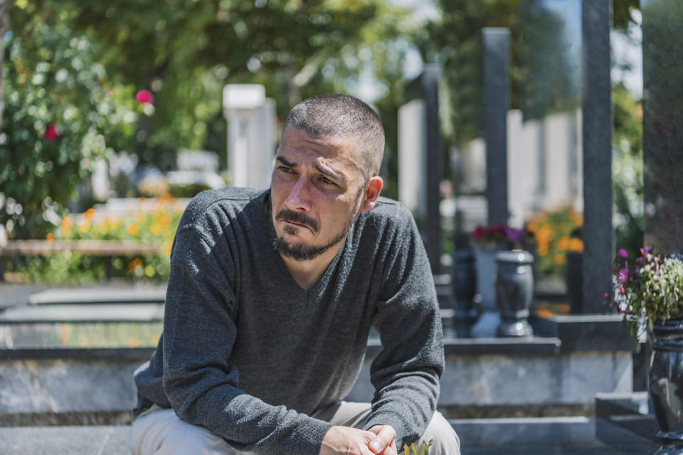 Man with short hair and beard sitting on steps in a garden area, appearing contemplative