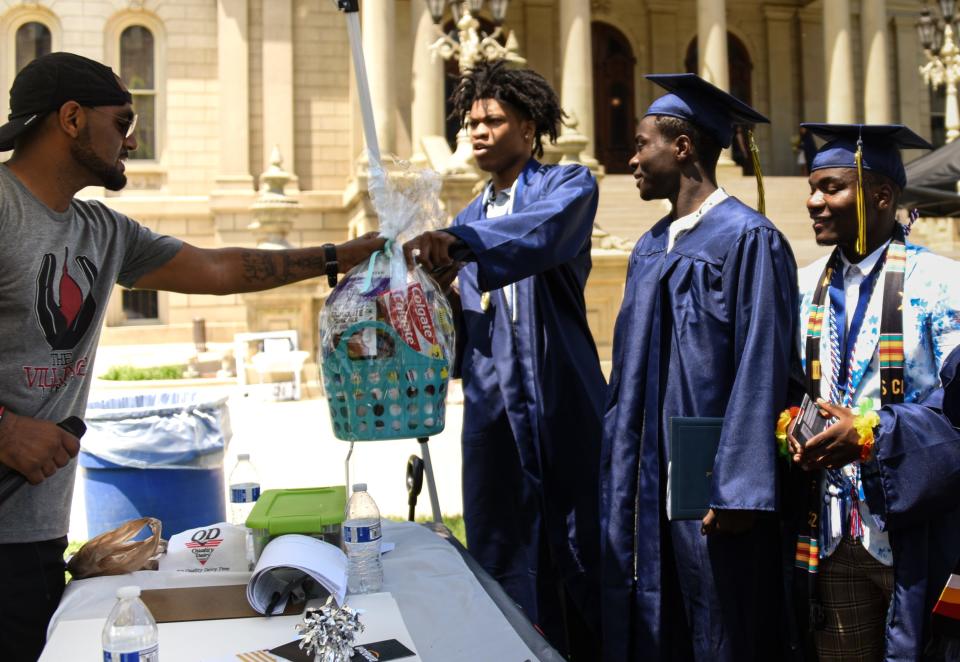 Michael Lynn, left, co-founder of The Village Lansing, hands out gifts to Lansing Eastern graduates Sunday during a graduation celebration at the Capitol. The Village Lansing is a nonprofit designed to empower youth and support families in Lansing.