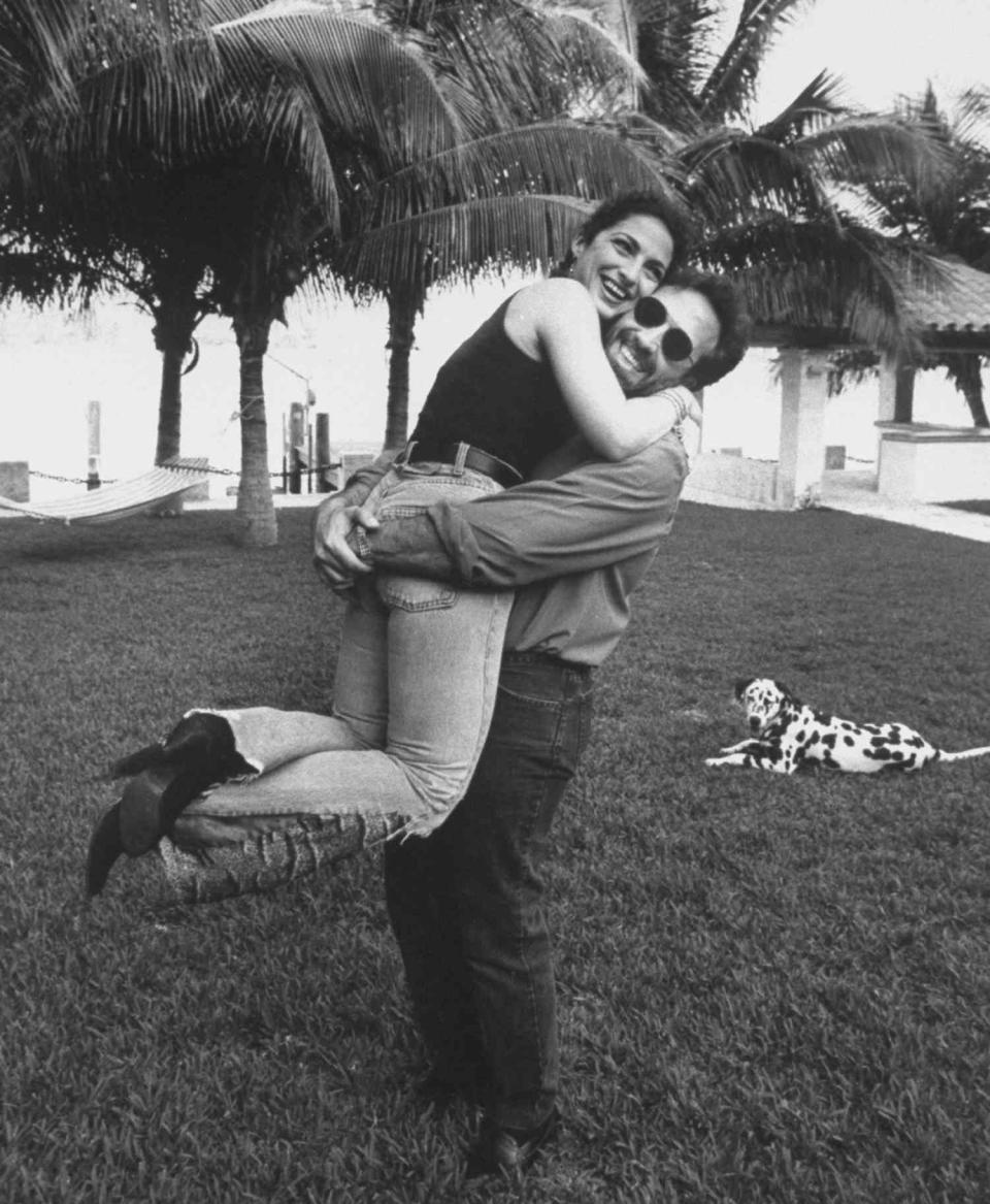 Gloria Estefan (L) jumping into the arms of husband Emilio after she recovered from accident which broke a vertebra in her spine, making a comeback w. their group Miami Sound Machine; at beachfront home w. dalmatian in background