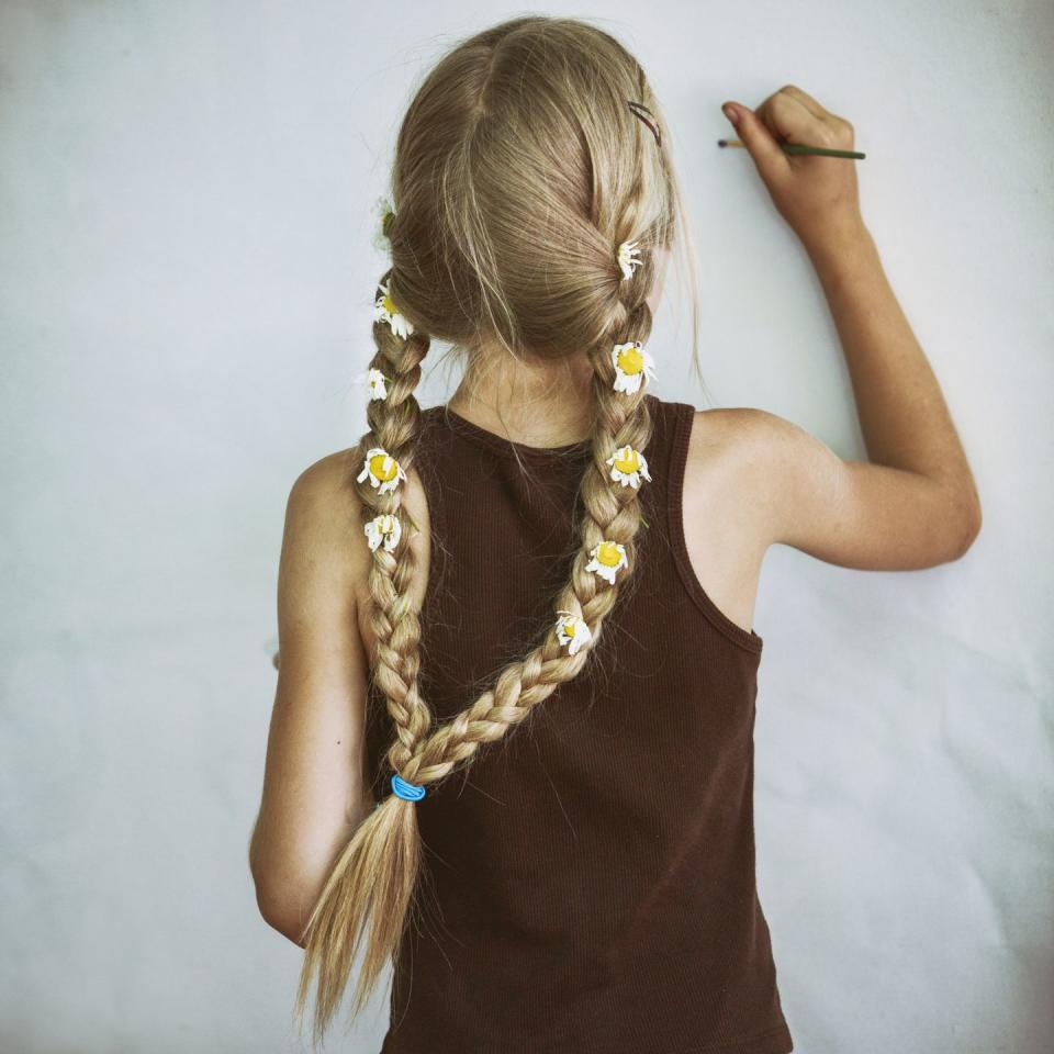 a young girl with long blonde hair at a fairy festival shown from the back while doing are work on a mural shows both braids with the flower detail