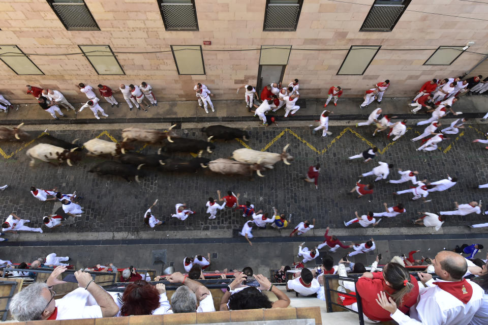 People run through the street with fighting bulls at the San Fermin Festival in Pamplona, northern Spain, Friday, July 8, 2022. Revellers from around the world flock to the city every year for nine days of uninterrupted partying in Pamplona's famed running of the bulls festival which was suspended for the past two years due to the coronavirus pandemic. (AP Photo/Alvaro Barrientos)