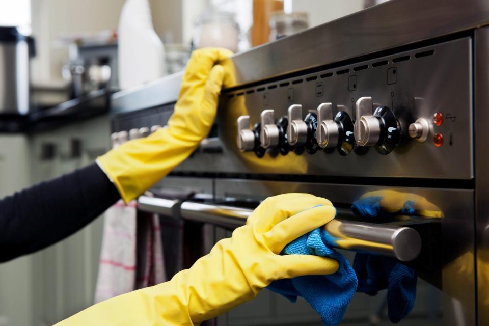 closeup photograph of two hands cleaning oven in a domestic kitchen