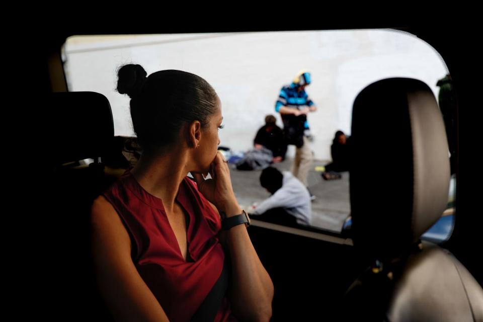 A woman looks out a car window at people on a sidewalk