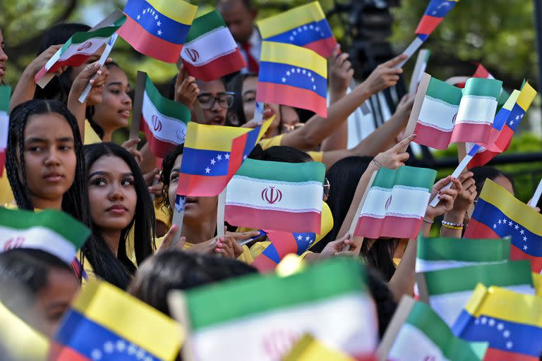 Mujeres jóvenes ondean banderas nacionales de Venezuela e Irán durante la llegada del presidente iraní Ebrahim Raisi al Palacio Presidencial de Miraflores en Caracas, el 12 de junio de 2023.