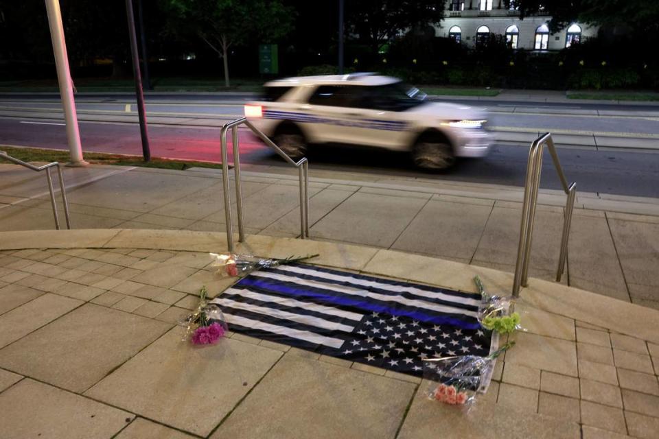 A memorial of a thin blue line flag with four bouquets are seen in front of the CMPD headquarters in uptown Charlotte Monday night, April 29, 2024. Fourth law enforcement officer dies, 4 wounded serving warrant in east Charlotte home Early in the day.