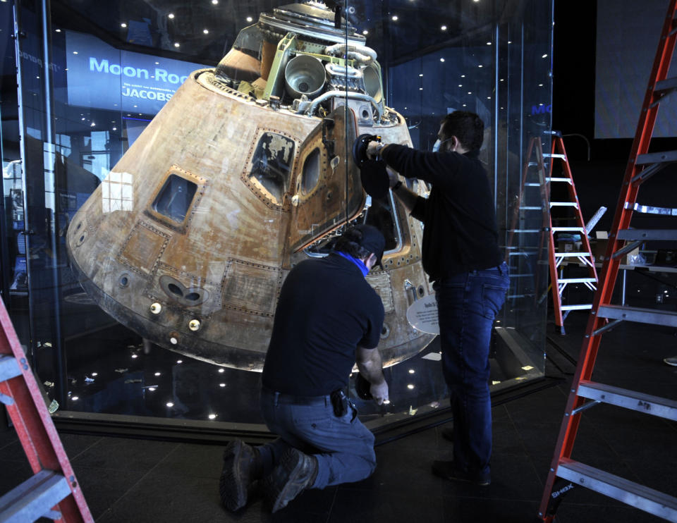 Workers open the glass case enclosing the Apollo 16 lunar capsule at the U.S. Space and Rocket Center in Huntsville, Ala., on Tuesday, Feb. 1, 2022. Following a break in routine maintenance because of the COVID-19 pandemic, the museum is sprucing up the antique spaceship before events marking the 50th anniversary of its flight to the moon in 1972. (AP Photo/Jay Reeves)