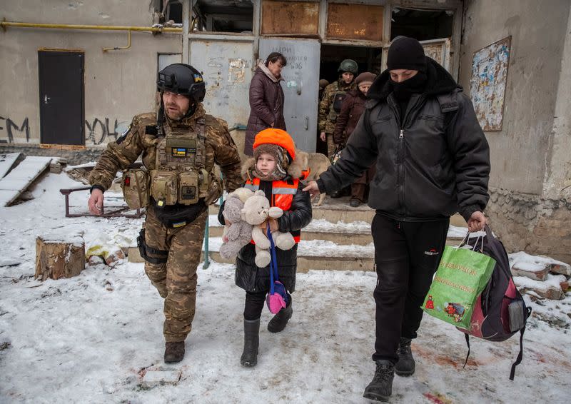 Policemen help Arina, 6, dressed in children's bulletproof vest and helmet during her evacuation from front line city of Bakhmut