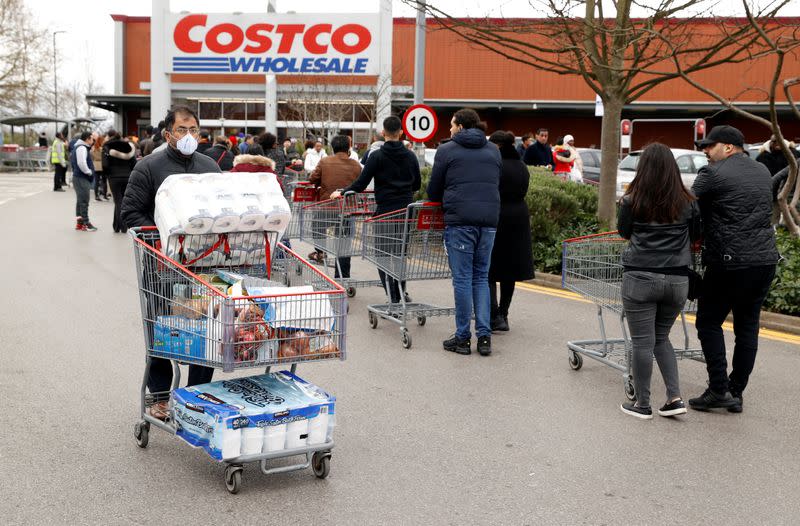 A masked customer leaves with shopping as other customers queue to enter a Costco Wholesalers in Chingford, Britain