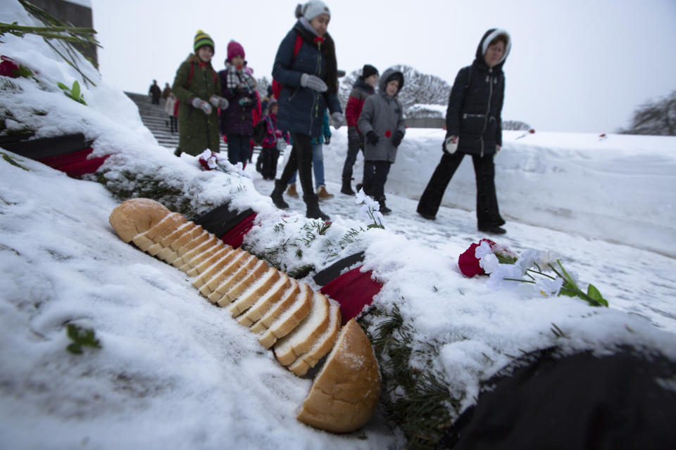 People walk past pieces of bread lying at a bed of honor at the Piskaryovskoye Cemetery where most of the Leningrad Siege victims were buried during World War II, in St.Petersburg, Russia, Saturday, Jan. 26, 2019. People gathered to mark the 75th anniversary of the battle that lifted the Siege of Leningrad. The Nazi German and Finnish siege and blockade of Leningrad, now known as St. Petersburg, was broken on Jan. 18, 1943 but finally lifted Jan. 27, 1944. More than 1 million people died mainly from starvation during the 900-day siege. (AP Photo/Dmitri Lovetsky)