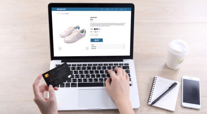a laptop displays a pair of white tennis shoes while one hand types on the laptop and another holds a credit card. stocks to buy from IBD’s Top 50