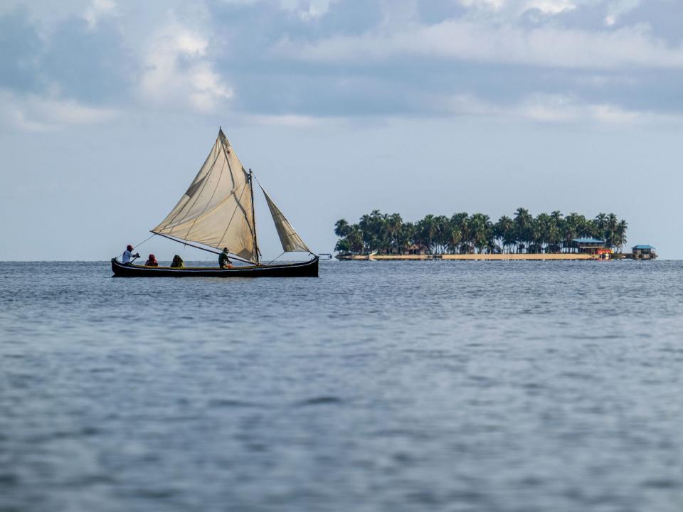 A Guna man transports his family on a boat with a sail near the island of Carti Sugtupu, not the island pictured in the distance.