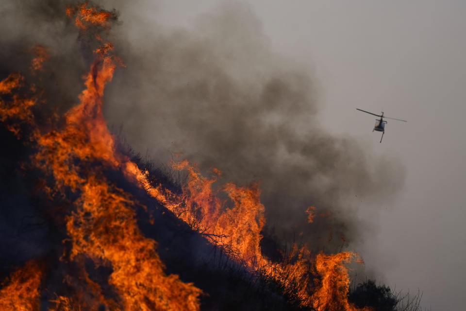 A helicopter flies away after dropping water over the Blue Ridge Fire burning along the 71 state highway Tuesday, Oct. 27, 2020, in Chino Hills, Calif. Crews tried to beat back two out-of-control wildfires in Southern California on Tuesday that have kept tens of thousands of people out of their homes even as another round of dangerous fire weather raises the risk for flames erupting across the state. (AP Photo/Jae C. Hong)