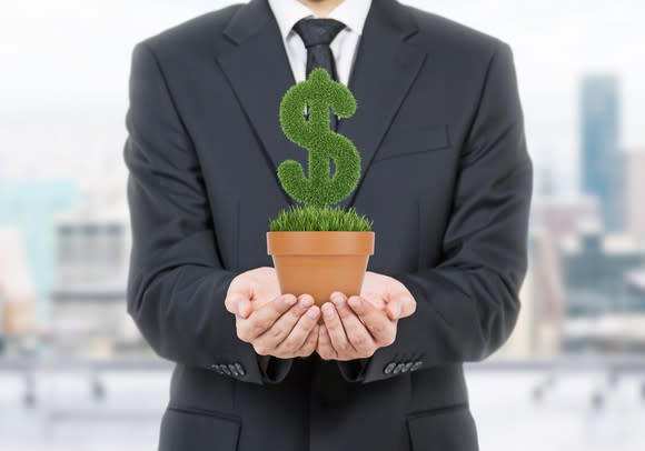 A businessman holding a potted plant that's shaped like a dollar sign.