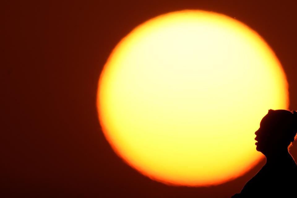 FILE - A woman is silhouetted against the setting sun as triple-digit heat indexes continue in the Midwest, Aug. 20, 2023, in Kansas City, Mo. The rate Earth is warming hit an all-time high in 2023 with 92% of last year’s surprising record-shattering heat caused by humans, top scientists calculated. (AP Photo/Charlie Riedel, File)